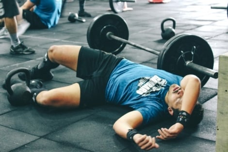 a fitness guy down on the ground tired after weight lifting exercises 