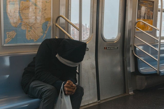 seated man bent over with hands clasped on subway train