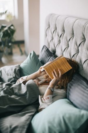 woman in bed covering face with book