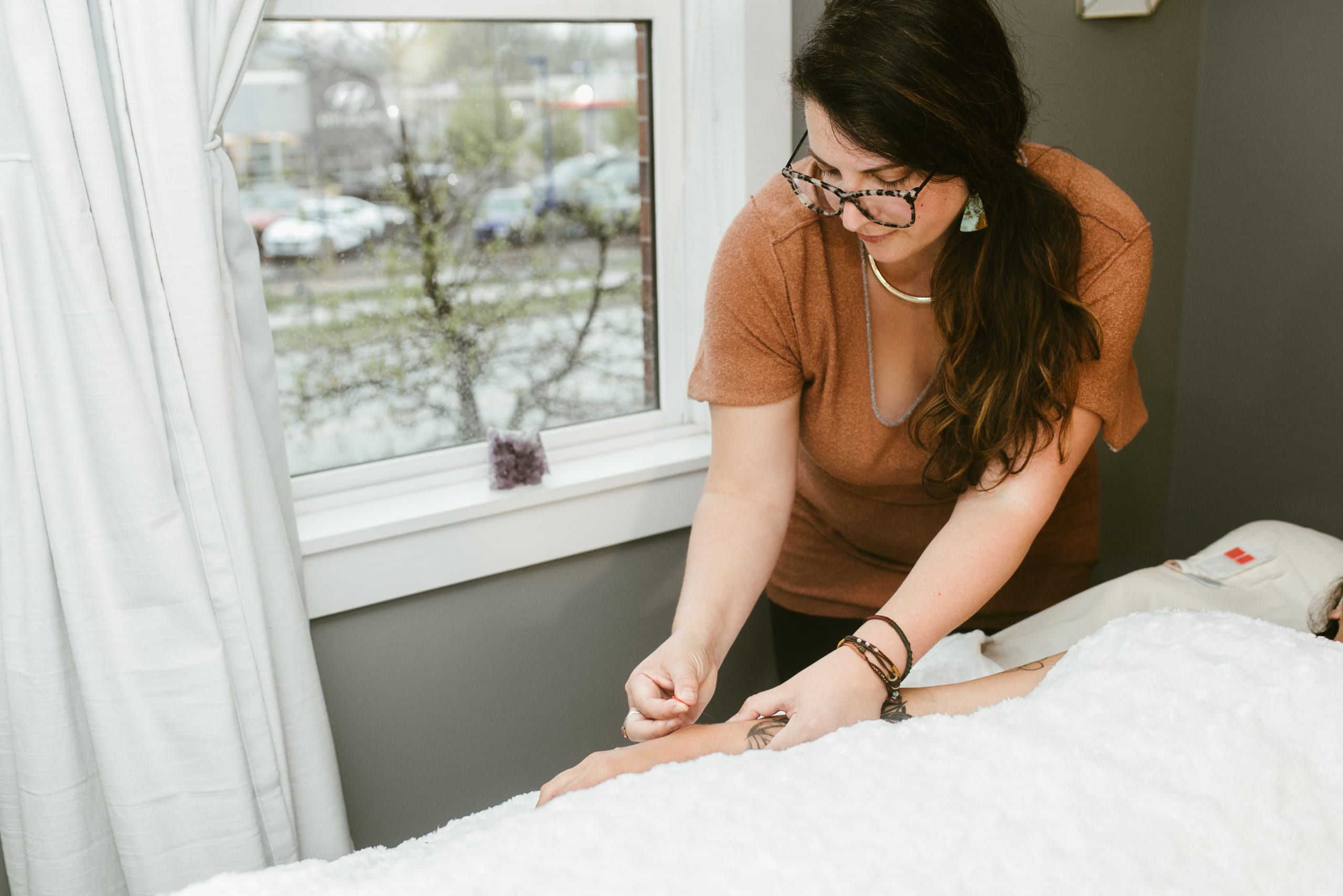 Rachel Muich inserts acupuncture needle into arm of woman on treatment table 