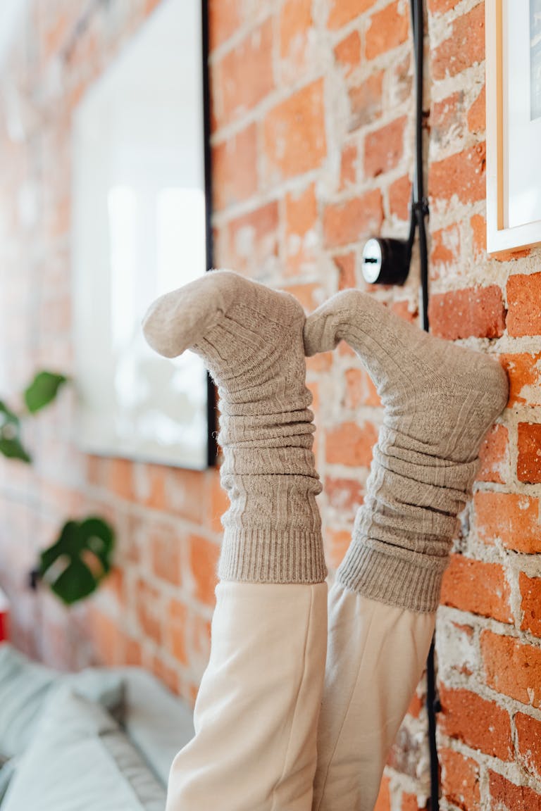 Comfortable feet in warm socks relaxing against a rustic brick wall.